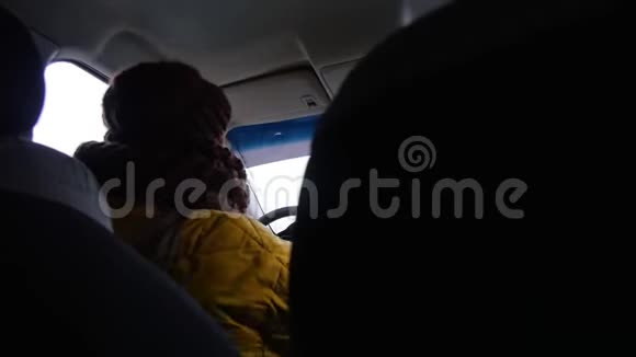 一位穿着黄色夹克的年轻女子坐在司机座位上放下面罩看着镜子检查她情况视频的预览图