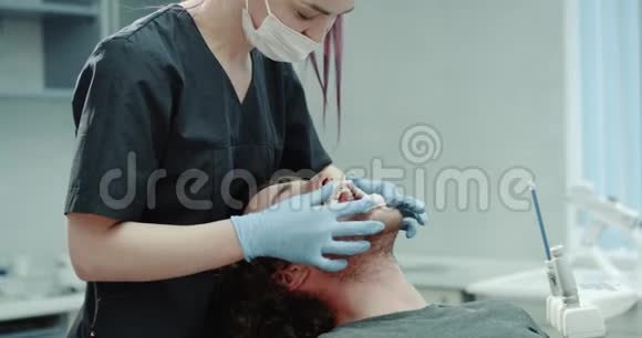 在一家现代化的牙科诊所里牙医把护口器固定在病人身上他滑稽地直视着摄像机视频的预览图