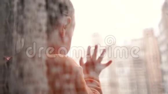 一个金发小男孩站在窗台上望着窗外视频的预览图