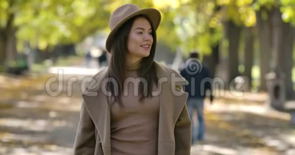 美丽的白种人女孩戴着优雅的棕色帽子和外套在秋天公园的背景上摆姿势积极的欧洲妇女视频的预览图