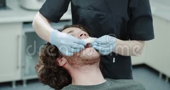 牙医的女人在牙科诊所的房间里给病人放了一个护口器快乐的病人坐在牙科椅上视频的预览图
