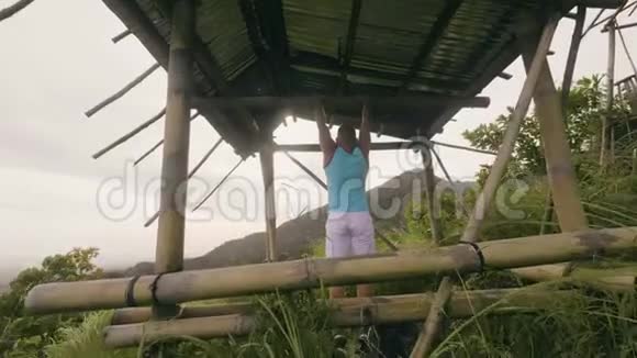 在热带自然背景下年轻人在横杆上训练腹部肌肉做腹肌训练的运动员视频的预览图