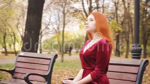 一个年轻女孩坐在公园的长凳上等待电话视频的预览图