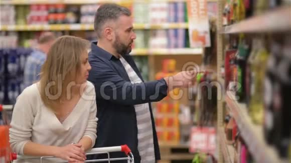 在超市购物快乐情侣年轻的家庭从超市货架上挑选葡萄酒视频的预览图