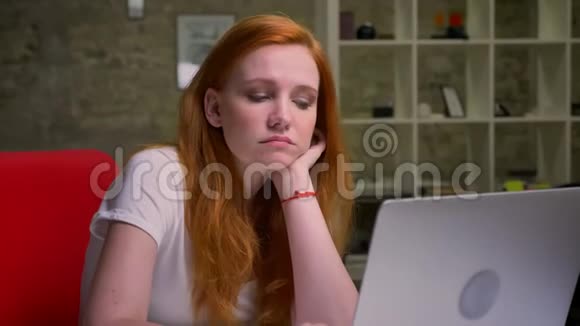 无聊的白种人白种人妇女坐在室内的笔记本电脑附近的工作场所轻砖背景视频的预览图