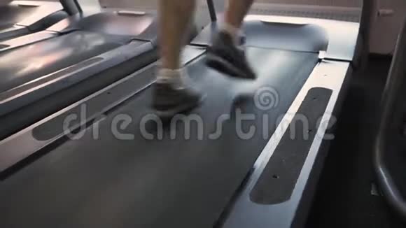 在健身室的跑步机上奔跑的无法辨认的男人的腿近距离后退低角度拍摄日落视频的预览图