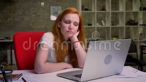 年轻的白种人红头发的女性正在看手提电脑屏幕而坐在桌面上的砖块办公室里有创意视频的预览图