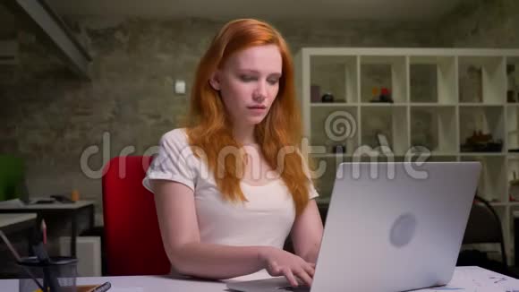 可爱的工作白种人生姜女孩坐着在她的桌面上点着屏幕轻盈的现代砖办公室视频的预览图