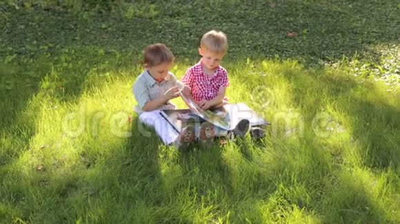 两个弟弟坐在公园的草地上看相册视频的预览图