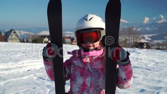 小女孩戴着白色的头盔穿着户外服装在阳光下手持高山滑雪板视频的预览图