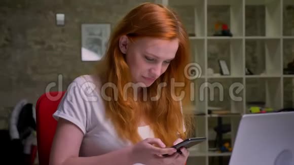 笑得令人敬畏的白种人红发女性正仔细地看着笔记本电脑坐在椅子上办公室插图视频的预览图