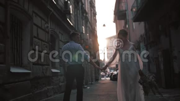 美丽浪漫的新婚夫妇新郎和新娘穿着华丽的礼服双手牵着手走着古老的街道视频的预览图