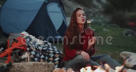 美丽迷人的女士晚上在篝火旁吃棉花糖视频的预览图