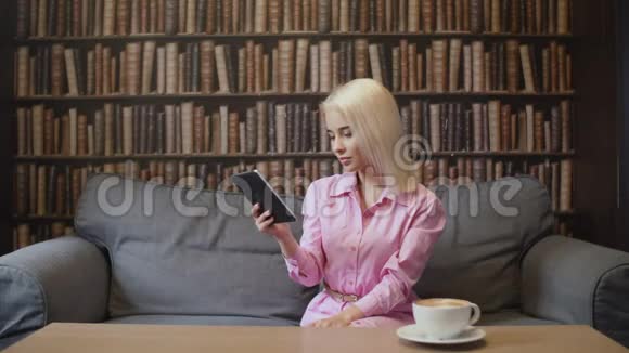 穿粉色衬衫的金发女人在咖啡馆里读电子书视频的预览图