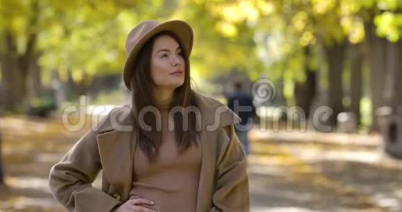 迷人的白种人女士戴着优雅的棕色帽子和外套摆在秋天公园的背景上积极的欧洲女孩视频的预览图