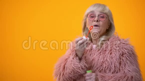 穿着粉红色外套和圆墨镜做肥皂泡的滑稽时髦奶奶广告视频的预览图