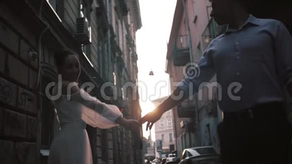 美丽浪漫的新婚夫妇新郎和新娘穿着华丽的礼服双手牵着手走着古老的街道视频的预览图