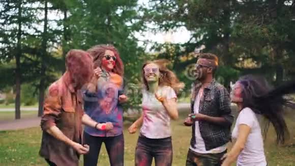 快乐的年轻人跳跃的慢动作然后在公园的Holi节上投掷粉末脸头发视频的预览图