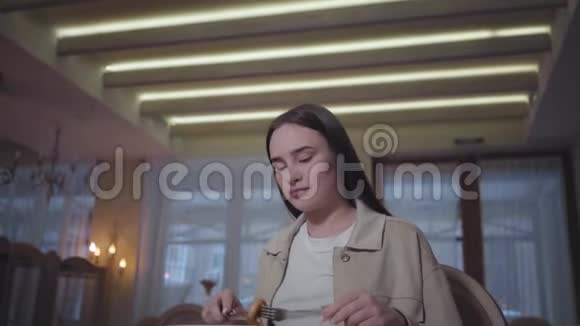 一位留着长发的漂亮女人坐在餐厅的桌子旁吃着小猪孤独的女士享受着这顿饭视频的预览图