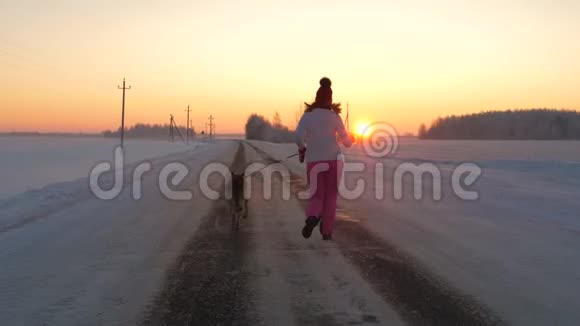 女人与狗在冬天的夜晚奔跑在迎接红霞日落的路上视频的预览图