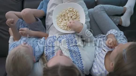 妈妈和两个孩子坐在沙发上吃爆米花看电视视频的预览图