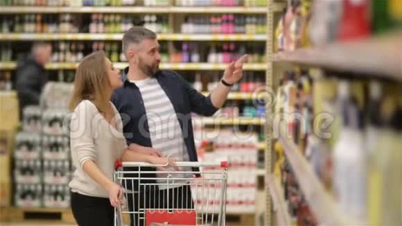 在超市购物快乐情侣年轻的家庭从超市货架上挑选葡萄酒视频的预览图