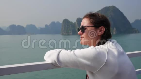 穿着白色夹克和太阳镜的年轻女子坐在船上看着海湾的美丽景色视频的预览图