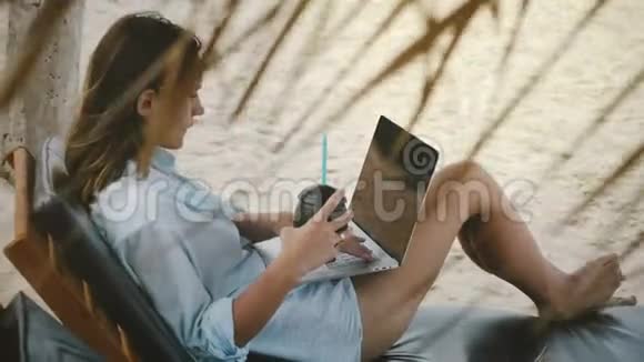 快乐美丽放松女性自由职业者与饮料工作使用笔记本电脑移动办公室在异国的海洋海滩视频的预览图