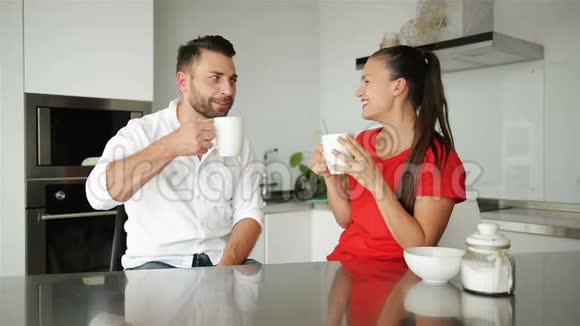 年轻夫妇在现代厨房吃早餐白色咖啡杯早上吃早餐幸福的妻子和丈夫浪漫浪漫视频的预览图
