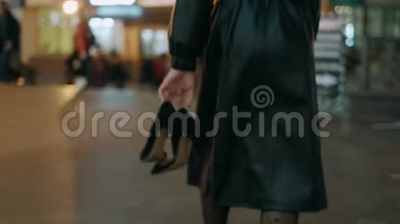 穿着黑色优雅外套的女人手里拿着高跟鞋光着脚沿着城市的夜街走特写视频的预览图
