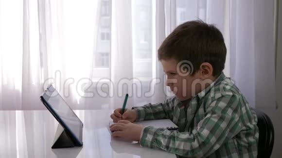 学前教育儿童男孩使用平板电脑进行家庭教学并在笔记本上做笔记视频的预览图