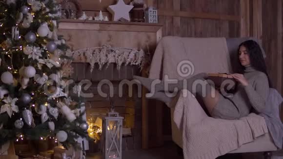 在圣诞节那天女孩拿着礼物打开盒子坐在圣诞树附近的椅子上高兴高清高清视频的预览图