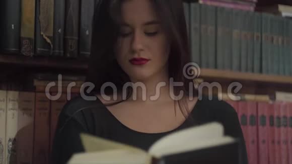 一个严肃的年轻学生的画像她的妆容鲜艳在图书馆书架前看书视频的预览图
