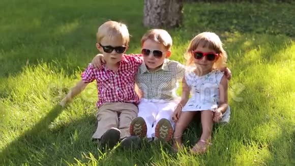 三个戴墨镜的小朋友坐在公园的草地上笑视频的预览图