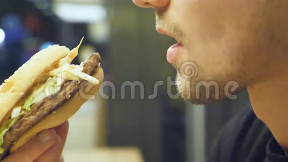 在购物中心的食品场吃大汉堡或芝士汉堡的年轻人的概况男性咬嘴和咀嚼视频的预览图