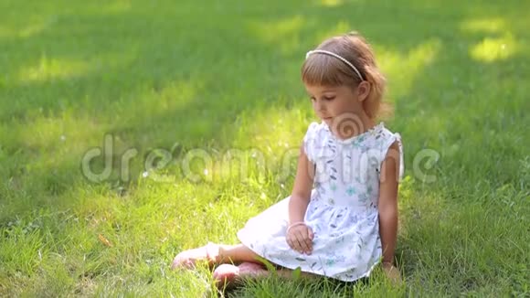 穿着夏装戴着发箍的小女孩坐在公园的绿草地上视频的预览图