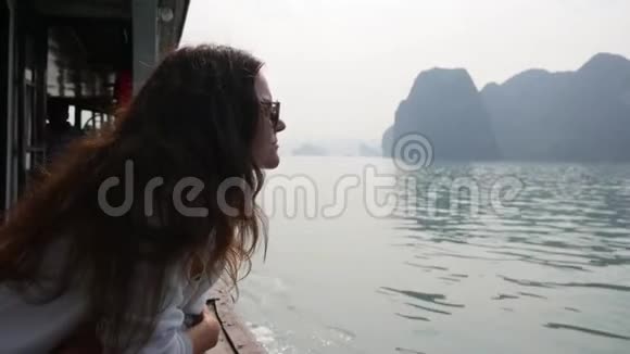穿着白色夹克和太阳镜的年轻女子坐在船上看着海湾的美丽景色视频的预览图