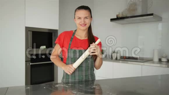 年轻的白人家庭主妇穿着条纹围裙厨房背景上隔离的红色T恤美丽的肖像视频的预览图