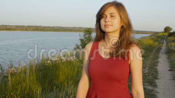 美丽的女孩在夕阳下带着芦苇沿着河岸散步可爱的女人在夏天的大自然中散步浪漫的心情视频的预览图