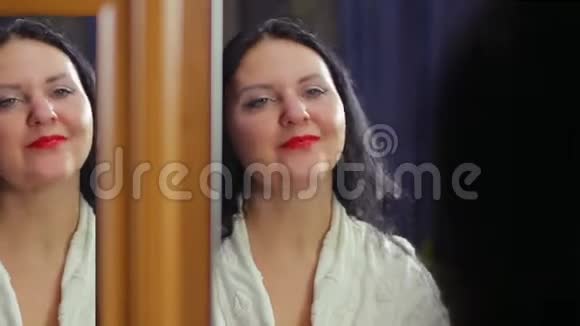 一个穿着白色长袍的年轻女人在镜子前涂着鲜红的口红微笑着用嘴唇调情视频的预览图