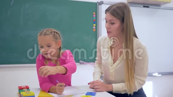 个人教育有经验的导师在学校教室黑板旁的桌子上教聪明的女孩视频的预览图