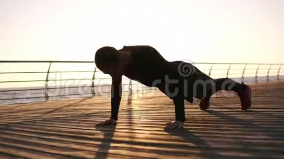 年轻的运动员在户外做俯卧撑在大海或海洋前的木制泡沫上拍手早晨的太阳健身视频的预览图