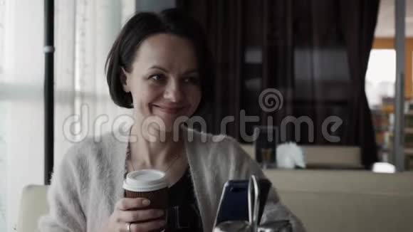 美丽的黑发女人从杯子里喝咖啡笑了视频的预览图
