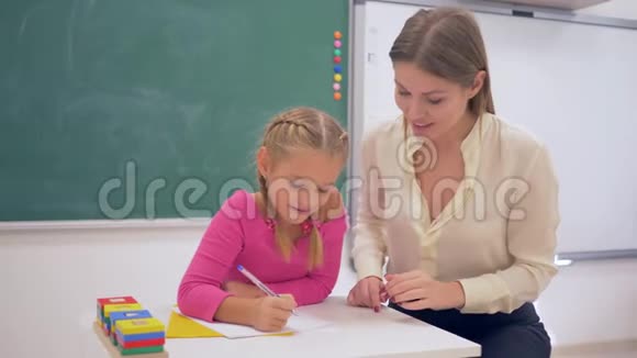 学校准备女教师帮助学习的女孩用黑板附近的桌子上的塑料图形获得知识视频的预览图