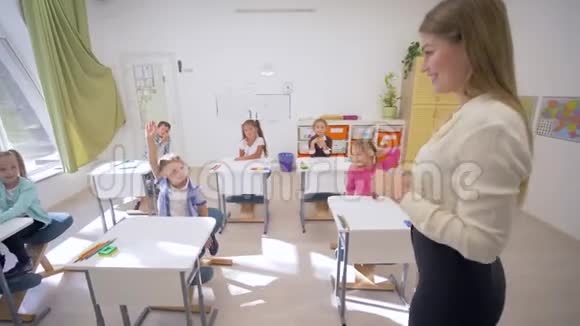 在学校的课堂上女老师在课桌前与可爱的孩子互动视频的预览图