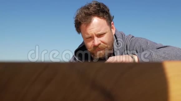 有胡子和胡子的木匠在蓝天上触摸桌子的表面由他手工制作手工手工制作视频的预览图