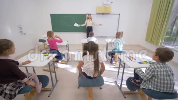 一群学童在上课时举手回答问题而坐在教师面前的课桌前板书视频的预览图