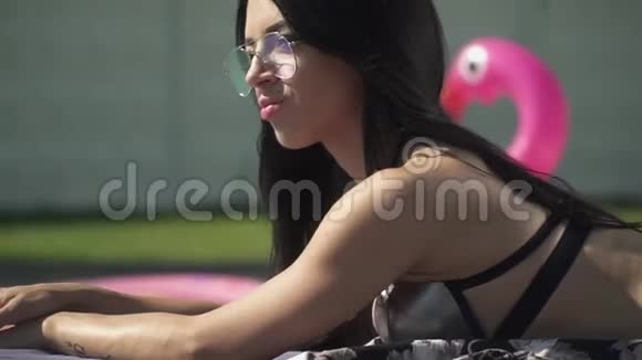 漂亮的年轻女人穿着泳装晒太阳穿比基尼戴太阳镜的可爱女士休闲视频的预览图