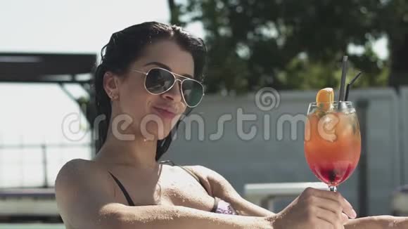 在游泳池里用鸡尾酒摆着墨镜的黑发女人的肖像穿比基尼的孤独女士的休闲视频的预览图