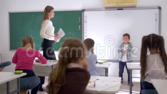 在教室里和老师一起坐在黑板旁听同学讲课的同学视频的预览图